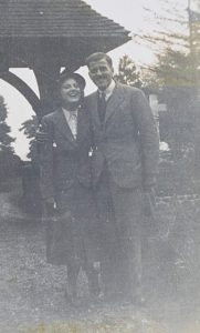 A young woman and a young man in 1940s daywear face the camera with big smiles. The photograph is creased and spotted from long wear.