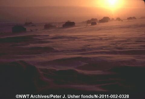 The sun on the horizon near the polar circle. Snow is visible in the foreground.